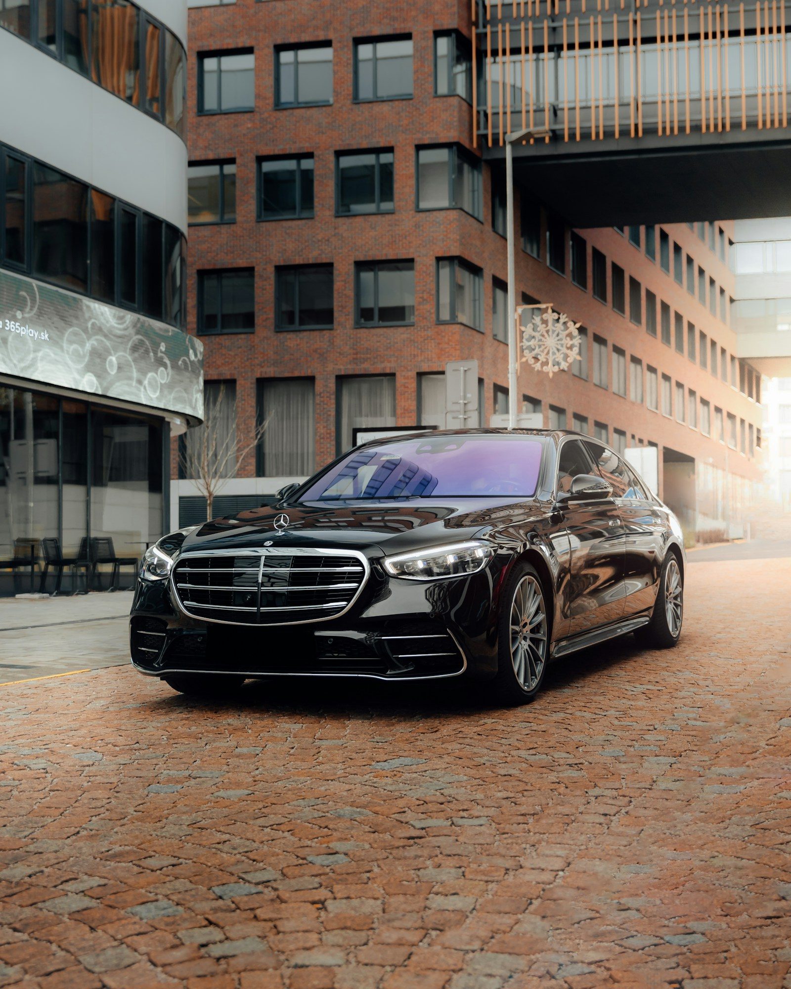 Một chiếc Mercedes S-Class màu đen đậu trên đường lát gạch giữa các tòa nhà